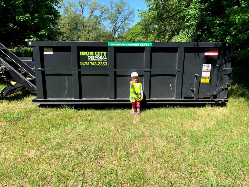 little girl in front of an Iron CIty Dumpster